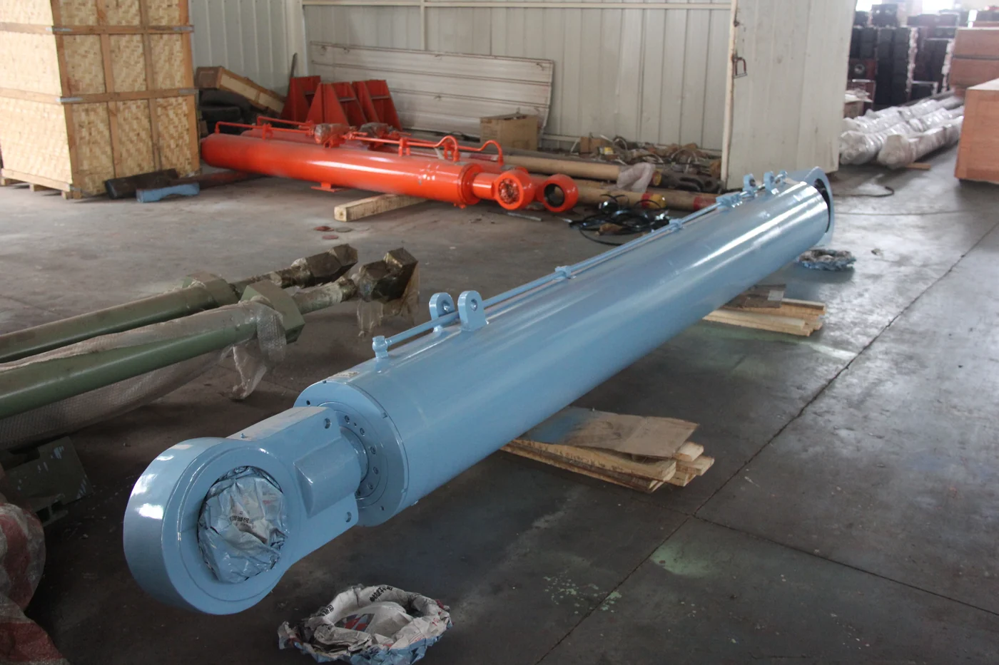 Long blue hydraulic cylinder with an eye mount and external piping