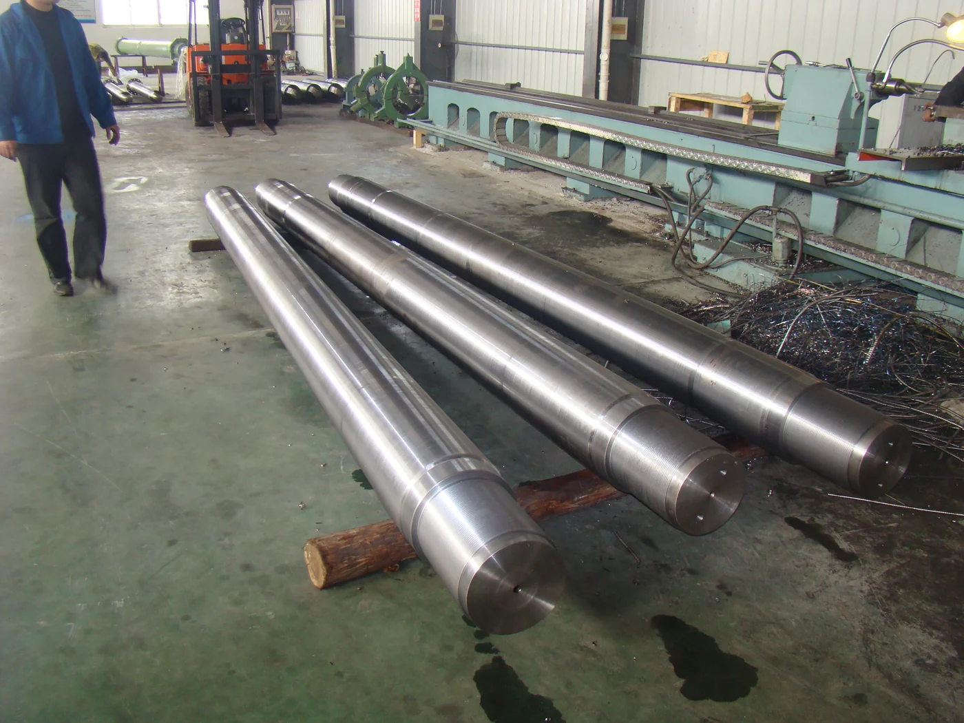 Long machined cylinder rod components supported beside workshop equipment