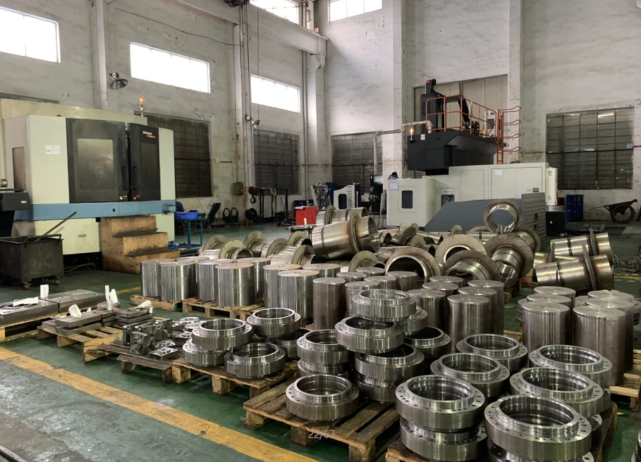 Machined cylindrical and flanged components on pallets beside machining equipment