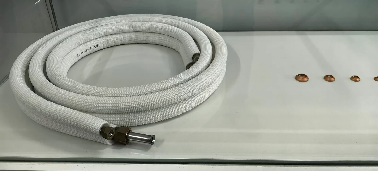Coiled tube assembly with white woven sleeving and metal end fittings on a workbench