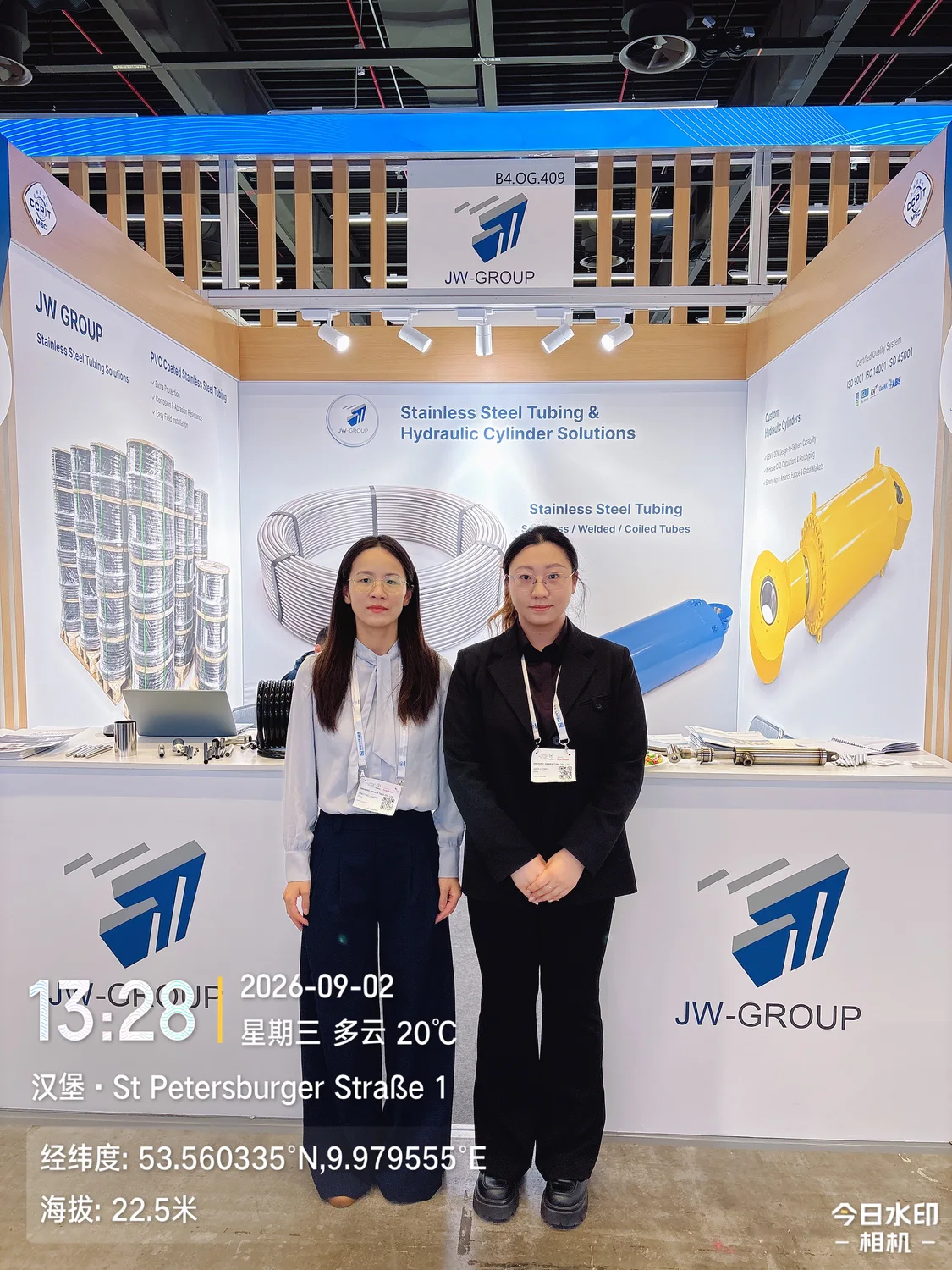 Two people standing in front of the JW-GROUP hydraulic cylinder and tubing exhibition display