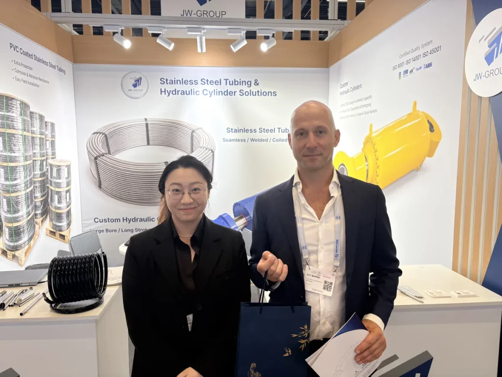 Two attendees at the JW-GROUP exhibition stand beside hydraulic cylinder and stainless steel tubing displays