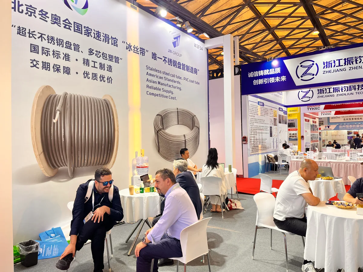 Visitors seated beside stainless steel coil and jacketed tubing graphics at the JW-GROUP exhibition stand