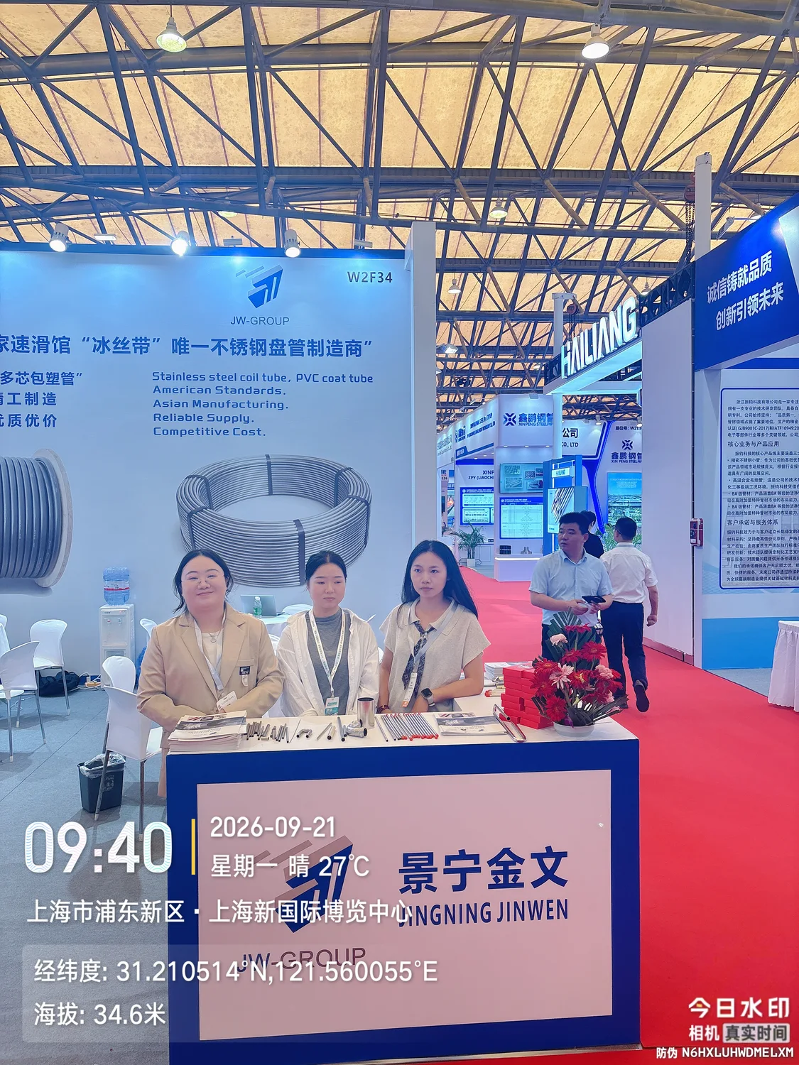 Three people at the JW-GROUP exhibition counter with straight tube samples and stand number W2F34 above